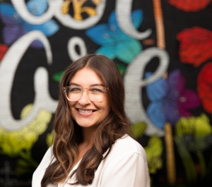Girl with glasses smiling in front of mural